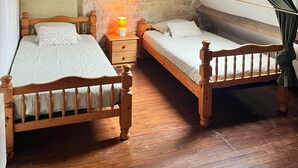 Un dormitorio con dos camas de madera, una pared de piedra, techo inclinado y tragaluz.