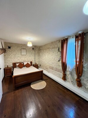 Een slaapkamer met een houten bed, stenen muren, een nachtkastje en een bedlampje.