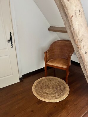 A room with a wooden chair, a woven rug, and a white door with a black handle.