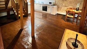 Un interior rústico con una escalera de madera, una zona de cocina con armarios blancos y una pared de piedra.