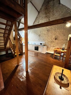 Een rustiek interieur met een houten trap, een keuken met witte kasten en een stenen muur.