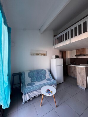 Una cocina compacta con refrigerador, una mesa de comedor con mantel estampado en azul, y una mesita redonda con revistas.