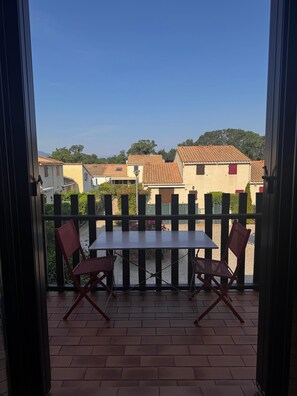 Varanda com mesa e cadeiras, vista para edifícios próximos e céu claro.