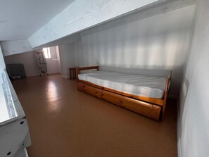 Uma cama de madeira simples num quarto com teto inclinado e radiador.