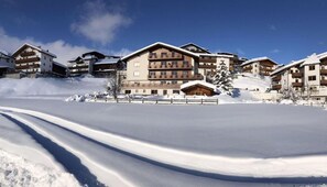 Une station de ski enneigée, avec des bâtiments à plusieurs étages, une piste de ski et un ciel dégagé.