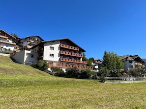 Un immeuble à plusieurs étages, doté de balcons, situé sur une pente herbeuse.