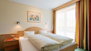 Habitació d'hotel amb un llit doble, una nitòria, una làmpada penjada a la paret i una finestra amb cortines.