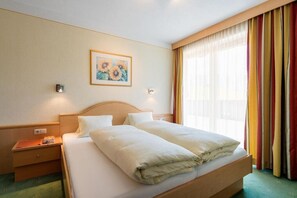 Une chambre d’hôtel avec un lit double, une table de chevet, une lampe fixée au mur et une fenêtre avec des rideaux.