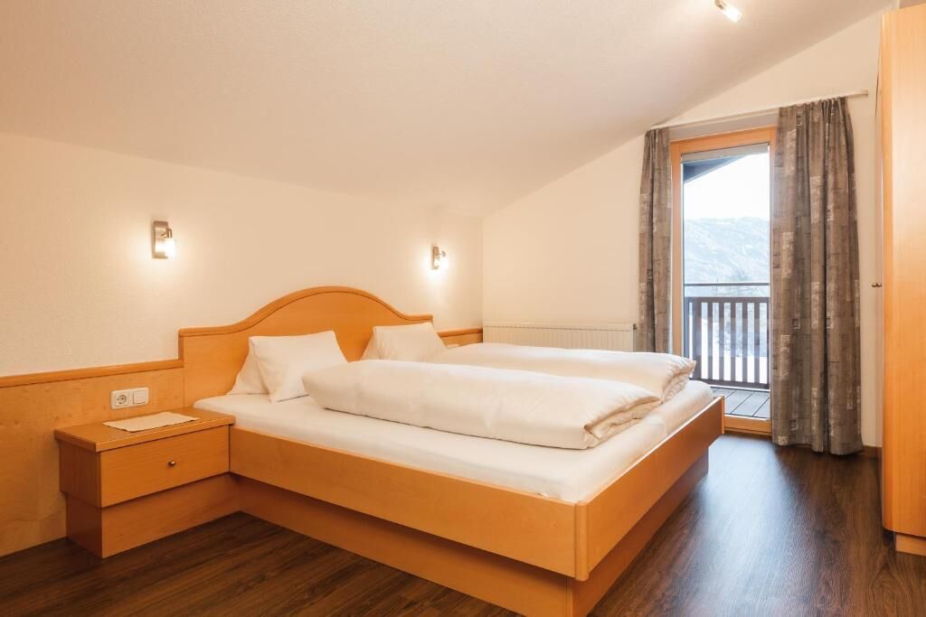 A double bed in a room with wooden flooring, a nightstand, and a window with curtains.