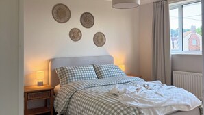 Un dormitorio con cama, mesitas de noche, lámpara colgante, ventana con cortinas y decoración en la pared.