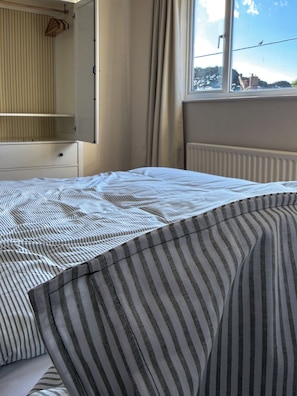 Een slaapkamer met een bed, een kast en een raam met uitzicht op gebouwen.