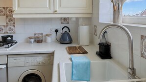 Una cocina con lavadora, hervidor y pileta con escurreplatos.