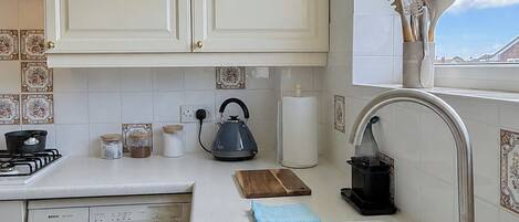 Una cocina con lavadora, hervidor y pileta con escurreplatos.