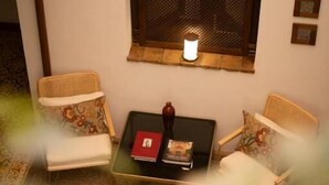 Una camera accogliente con una finestra, due poltrone in vimini, un tavolino con libri e un elemento decorativo al muro.