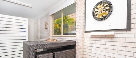 A room with a brick wall, a window with a view of greenery, and a dartboard on the wall.