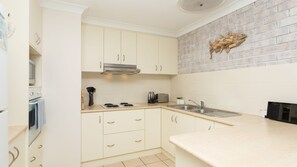 A kitchen with white cabinets, a brick backsplash, a stainless steel range hood, a sink, and a toaster. - Sunsets & Sand Iluka (Iluka)