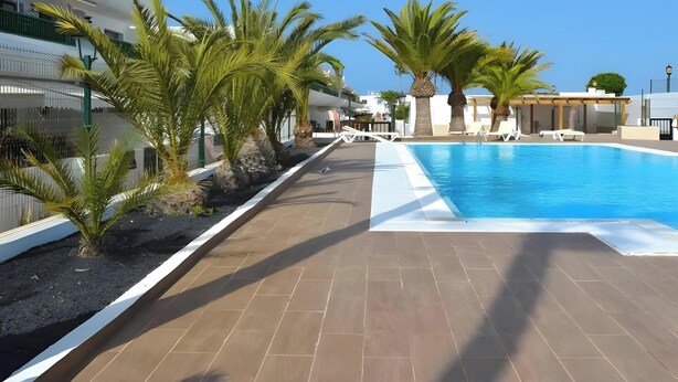 Area piscina con pavimento piastrellato, palme e cielo azzurro limpido.