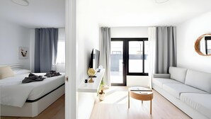 Una camera d'albergo moderna con un letto, un divano, una TV, un tavolino e un balcone con tende.