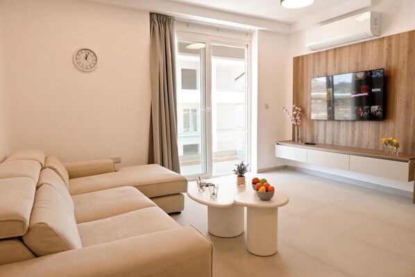 Een moderne woonkamer met een zithoek, een flatscreen televisie, een bijzettafeltje met een fruitschaal en een schuifpui.