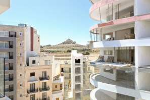 Een meerlaags appartementencomplex met balkons, uitzicht op een heuvel en bouwmateriaal op het dak.