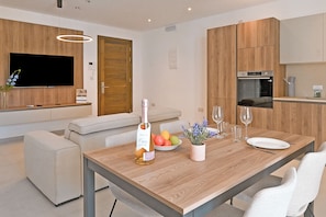 A modern kitchen with wooden cabinets, a built-in oven, and a dining area with a wooden table. - Modern Seaside Apart in Marsalforn - 5D, Marsalforn Iz-Zebbug Gozo, Malta (Marsalforn Iz-Zebbug Gozo)