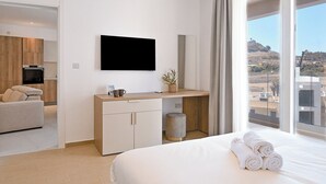 Et hotelværelse med en seng, et skrivebord med et fladskærms-tv, udsigt over landskabet og en lille plante på skrivebordet.