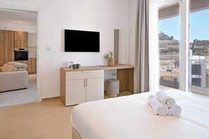 A hotel room with a bed, a desk with a flat-screen TV, a view of the landscape, and a small plant on the desk. - Modern Seaside Apart in Marsalforn - 5D, Marsalforn Iz-Zebbug Gozo, Malta (Marsalforn Iz-Zebbug Gozo)