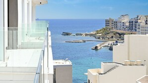 A coastal view from a balcony overlooking a marina with boats, rocky outcrops, and buildings. - Modern Seaside Apart in Marsalforn - 6A, Marsalforn Iz-Zebbug Gozo, Malta (Marsalforn Iz-Zebbug Gozo)