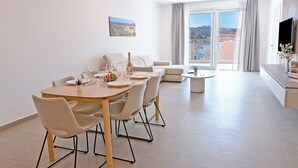 A modern living room with a dining area, a sofa, a TV, and a balcony with a city view. - Modern Seaside Apart in Marsalforn - 6A, Marsalforn Iz-Zebbug Gozo, Malta (Marsalforn Iz-Zebbug Gozo)