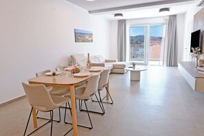 A modern living room with a dining area, a sofa, a TV, and a balcony with a city view. - Modern Seaside Apart in Marsalforn - 6A, Marsalforn Iz-Zebbug Gozo, Malta (Marsalforn Iz-Zebbug Gozo)