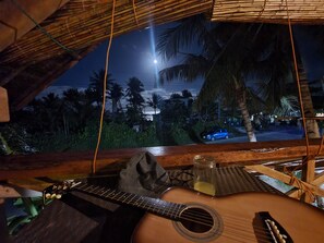 A wooden guitar, a glass jar, and a woven mat on a table with a view of palm trees and a car outside. - Coleto Siargao (Rodriguez)