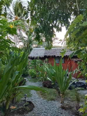 Un jardín tropical con una estructura de techo de paja, rodeado de exuberante follaje y un sendero de grava.