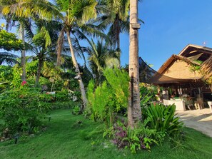 A tropical garden with palm trees, a thatched-roof structure, and lush greenery.