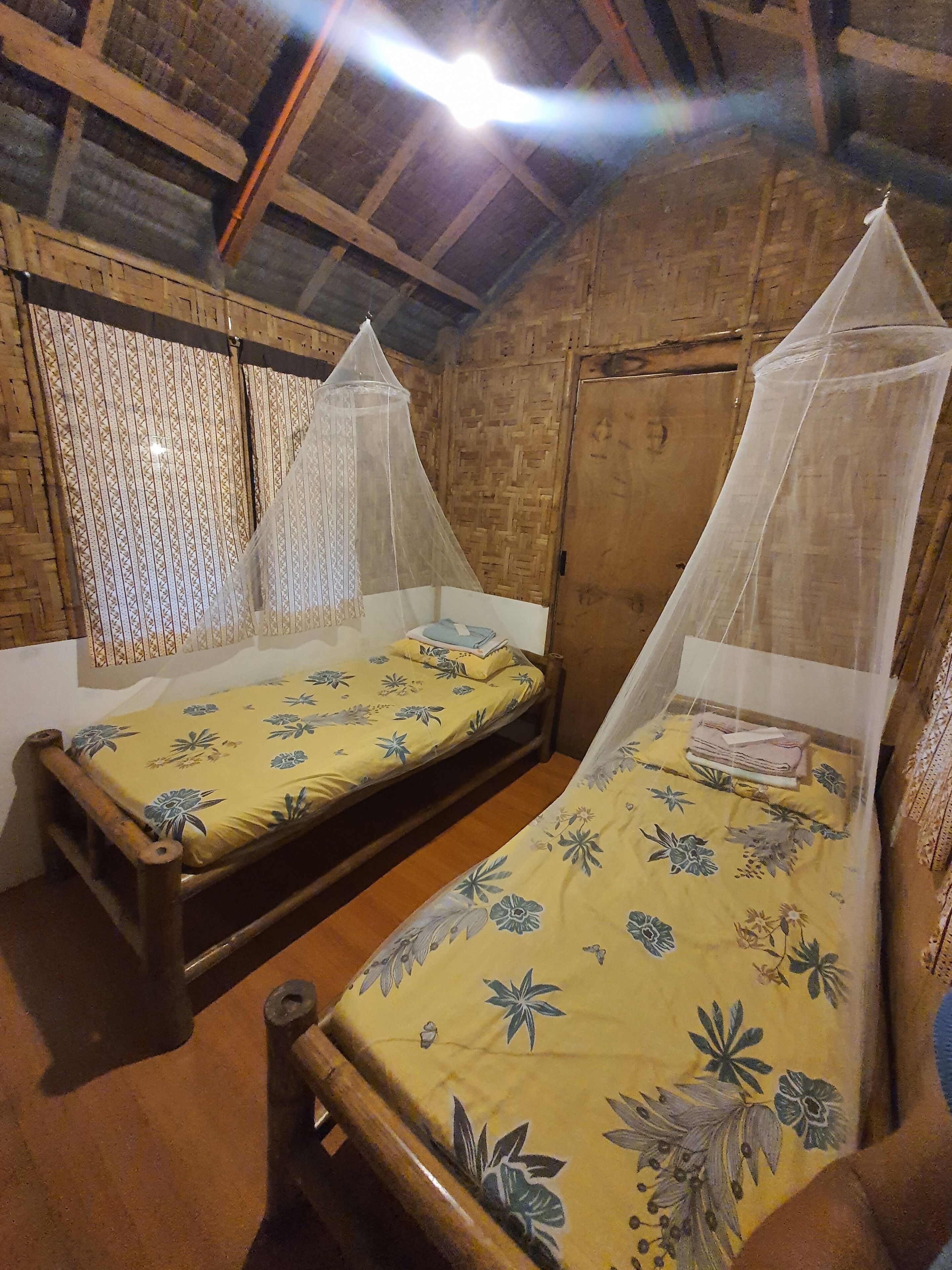 Two wooden beds with mosquito nets, a woven wall, and a wooden ceiling.