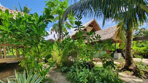 A tropical garden with a thatched-roof structure, lush greenery, and a clear sky. - Coleto Siargao (Rodriguez)