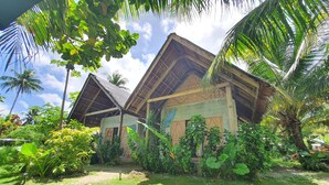 A traditional thatched-roof building surrounded by lush greenery and palm trees. - Coleto Siargao (Rodriguez)