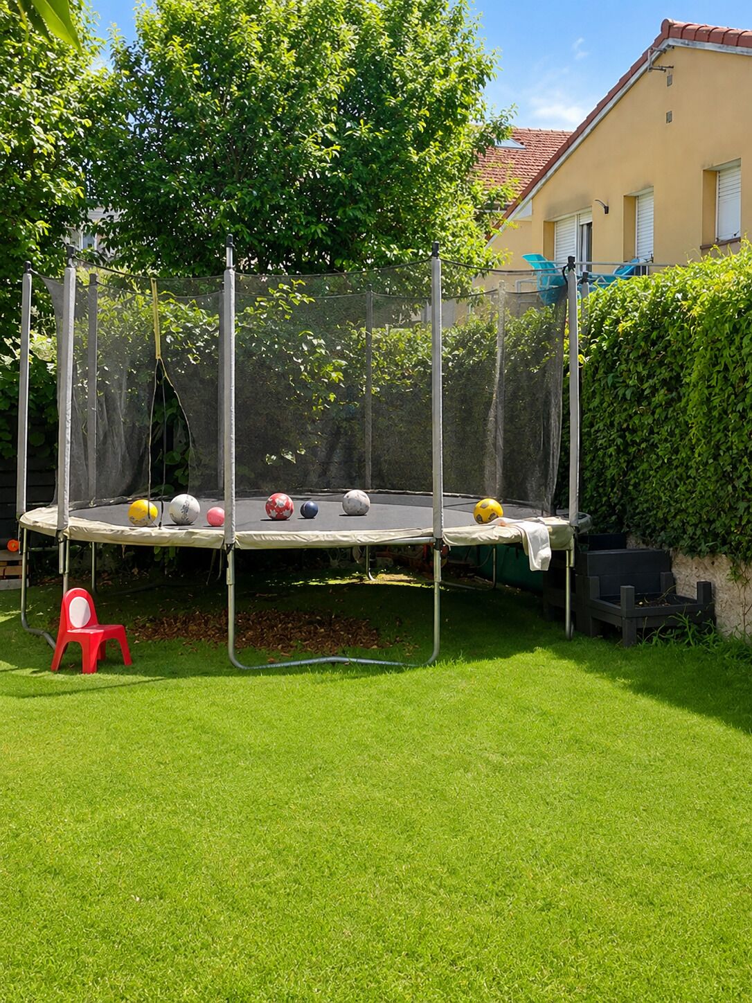 Un trampolín en un patio trasero con una silla roja y un seto.