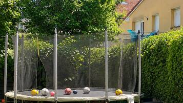 Un trampolín en un patio trasero con una silla roja y un seto.
