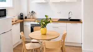 A modern kitchen with white cabinets, a round wooden table, and four chairs. - Chez Aurel et Ju (Tournon-sur-Rhône)