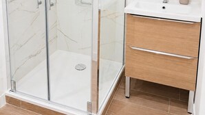 A modern bathroom with a glass-enclosed shower, a wooden vanity with a mirror, and marble-patterned walls. - Chez Aurel et Ju (Tournon-sur-Rhône)
