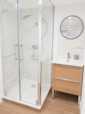 Een moderne badkamer met een glazen douchecabine, een houten wastafelmeubel met spiegel en wanden met een marmerprint.