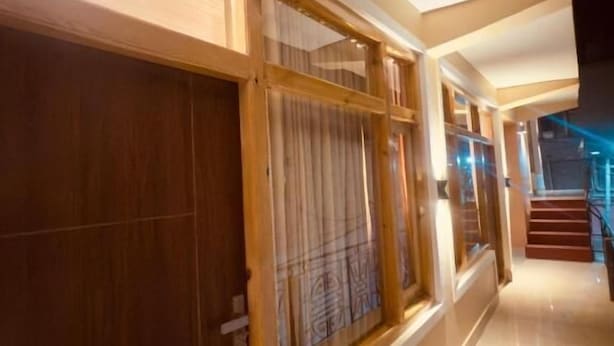 A hallway with wooden doors and glass panels, a tiled floor, and a staircase in the background. - Milam Hostel (Leh)