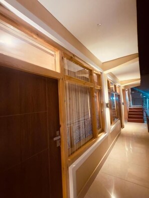 Un pasillo con puertas de madera y paneles de vidrio, suelo de baldosas y una escalera al fondo.