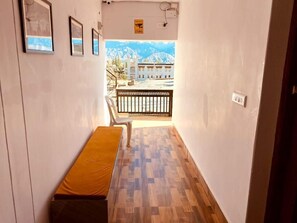 Un pasillo con un banco, cuadros en la pared y vista a un edificio con montañas al fondo.