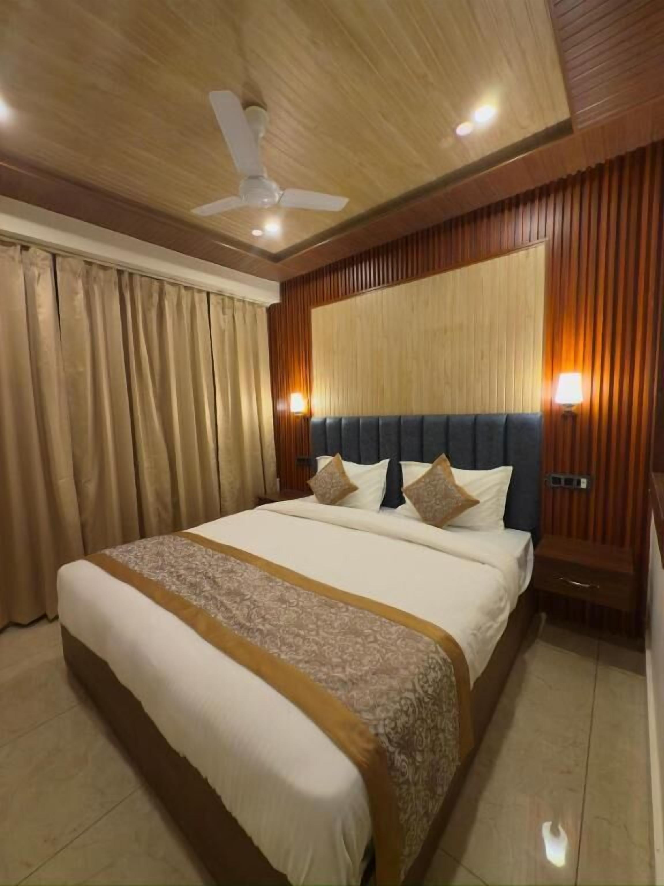 A hotel room with a large bed, wooden paneling, a ceiling fan, and two wall-mounted lamps.