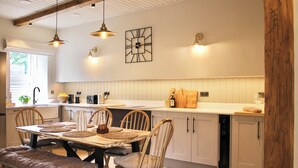 A kitchen with wooden cabinets, a dining table with chairs, pendant lights, and a clock on the wall. - The Stirling Lookout | Panoramic Terrace Views | Steps from Stirling Castle (Stirling)