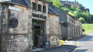 A stone building with a sign for 'Lower Castlehill' and 'Strange Distillery.' - The Stirling Lookout | Panoramic Terrace Views | Steps from Stirling Castle (Stirling)