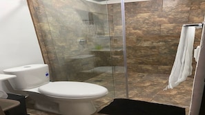Ein Badezimmer mit Toilette, einer gläsernen Duschkabine und Fliesenboden.