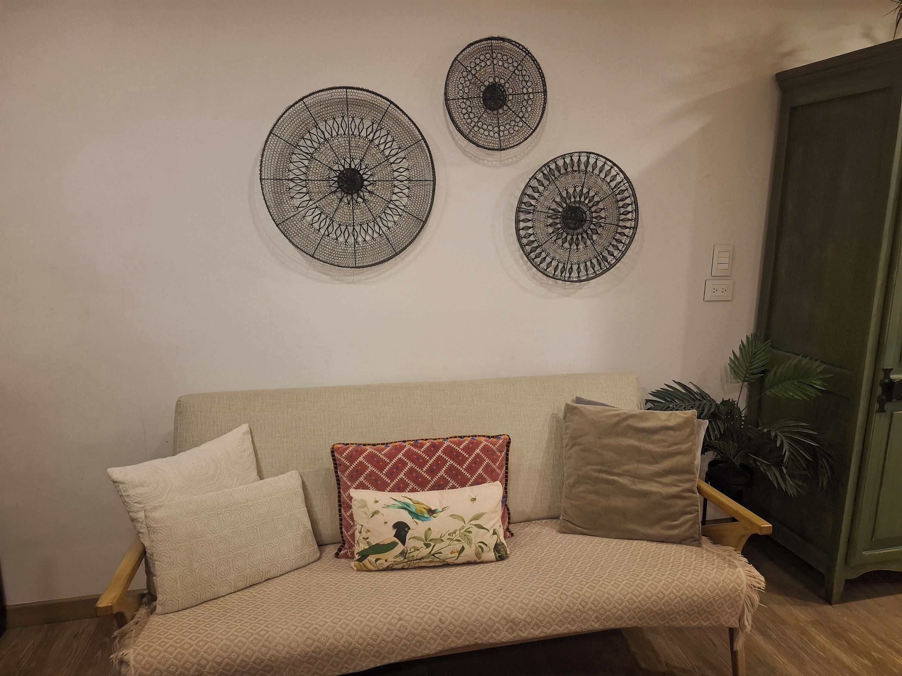 A beige sofa with patterned cushions, a wall-mounted circular decorative item, and a green cabinet.