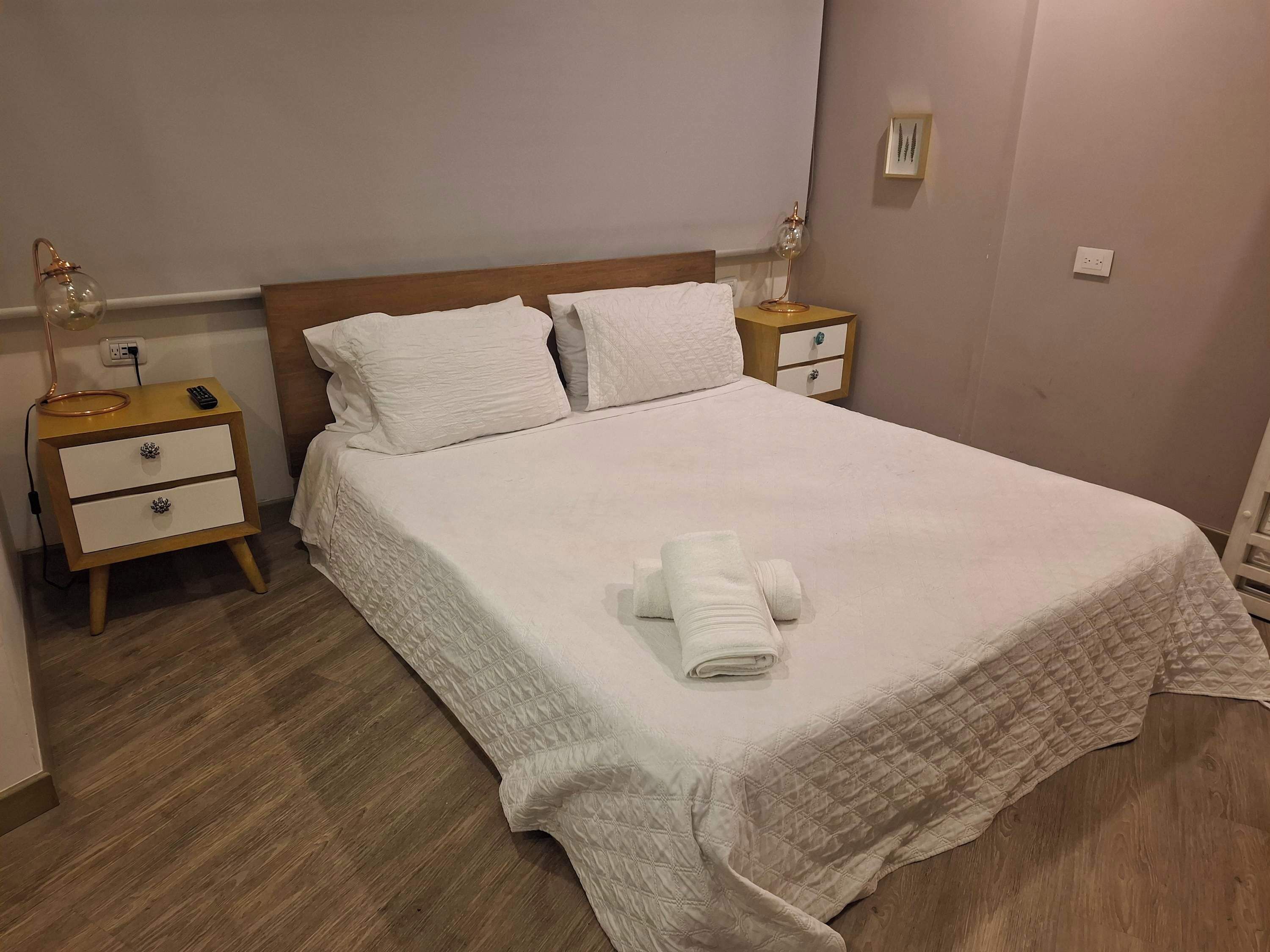 A neatly made bed with a quilted bedspread, two bedside tables with lamps, and a wooden floor.